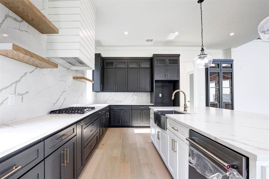 Kitchen featuring white cabinetry, light hardwood / wood-style flooring, backsplash, stainless steel appliances, and hanging light fixtures