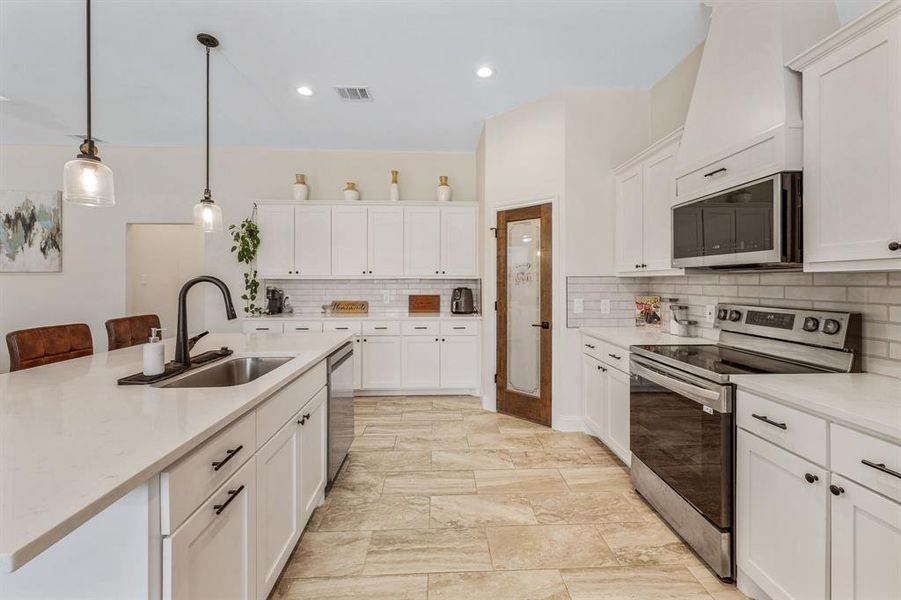 Kitchen featuring appliances with stainless steel finishes, pendant lighting, a kitchen bar, light stone countertops, and recessed lighting Kitchen featuring appliances with stainless steel finishes, pendant lighting, a kitchen bar, light stone countertops, and recessed lighting