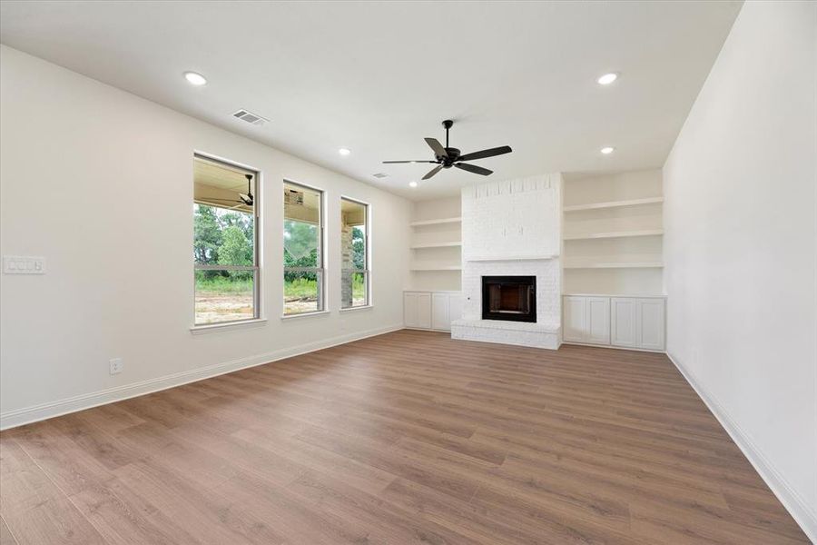 Unfurnished living room with hardwood / wood-style flooring, a brick fireplace, built in shelves, and ceiling fan