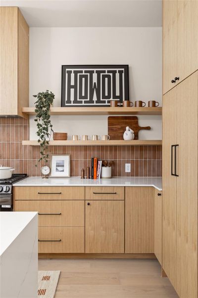 Kitchen featuring light brown cabinetry, open shelves, tasteful backsplash, stainless steel gas stove, and light wood-style flooring