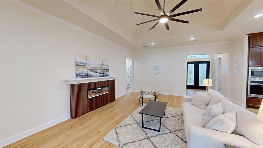 Living area featuring a raised ceiling, a ceiling fan, recessed lighting, light wood finished floors, and a glass covered fireplace