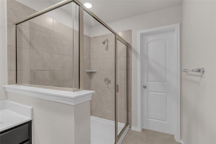 The photo depicts a modern bathroom with a walk-in shower enclosed by a glass door, neutral beige tiling.