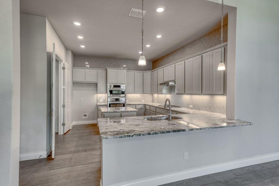 Kitchen featuring wood finished floors, recessed lighting, light stone counters, a peninsula, and backsplash