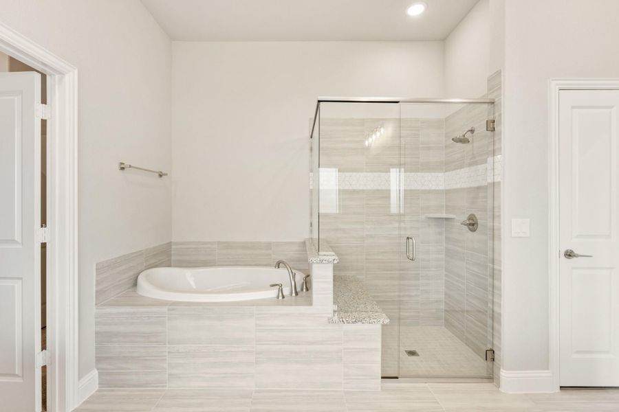 Master bathroom with soaking tub, glass-enclosed shower, and light gray tile floors and walls