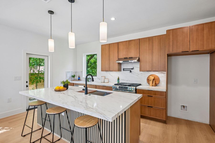 Modern kitchen with large island, sleek wooden cabinetry, pot filler and stainless steel appliances. Modern kitchen with large island, sleek wooden cabinetry, pot filler and stainless steel appliances.
