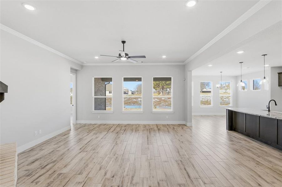 Unfurnished living room featuring light wood-style flooring, ornamental molding, healthy amount of natural light, a ceiling fan, and recessed lighting