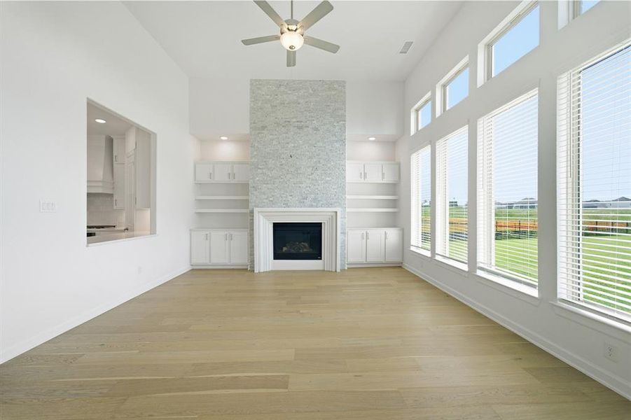 Spacious living area featuring high ceilings, wood-finish flooring, a contemporary fireplace with a textured tile surround, built-in shelving, and tall windows with blinds