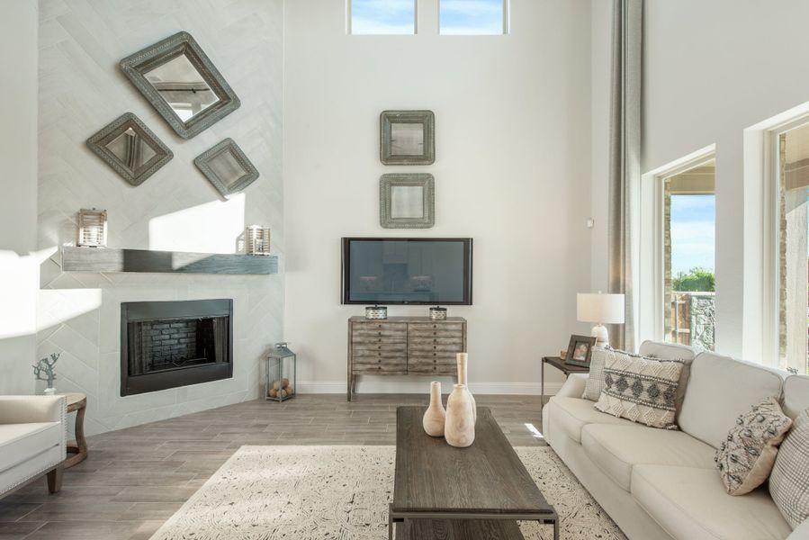 Living room with high ceilings, white fireplace, gray wood floors, and neutral sofa with decorative mirrors on the wall