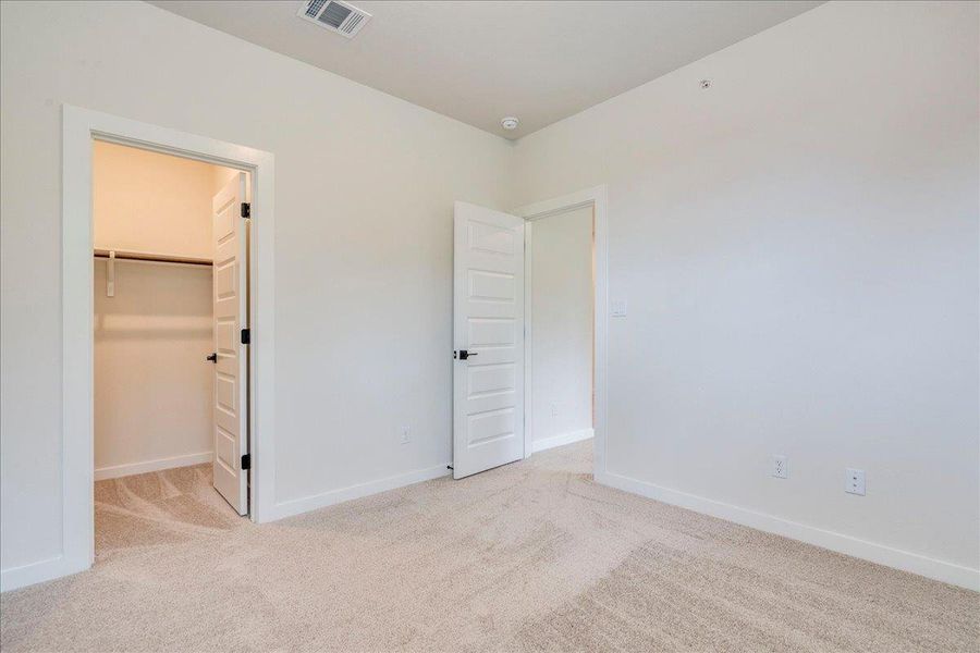 An airy bedroom with soft carpet flooring and a spacious walk-in closet.