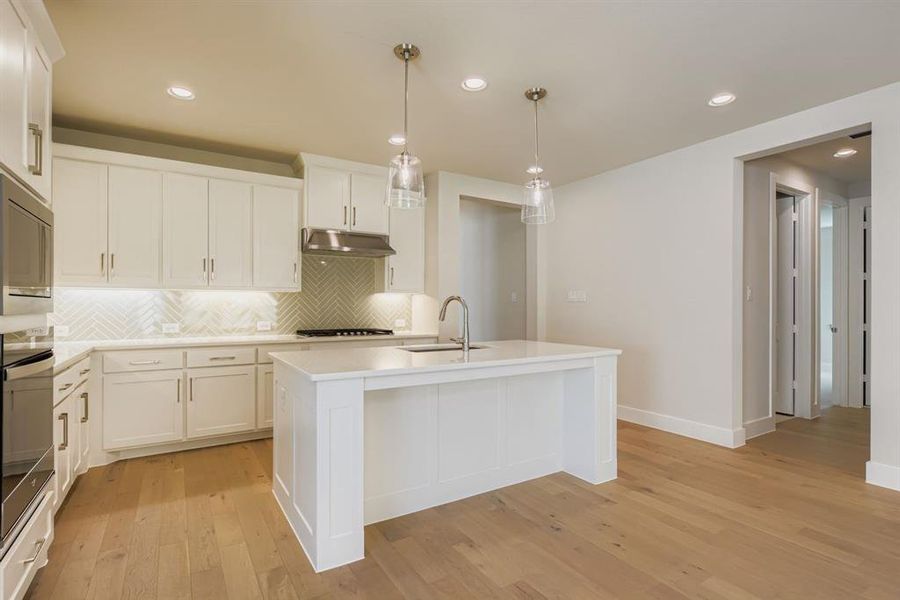 Kitchen with backsplash, recessed lighting, decorative light fixtures, light wood-style flooring, and a center island with sink