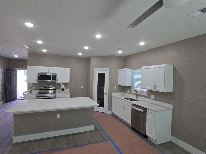 Kitchen featuring an expansive island with a light-toned countertop, stainless steel appliances, white cabinetry, and recessed lighting
