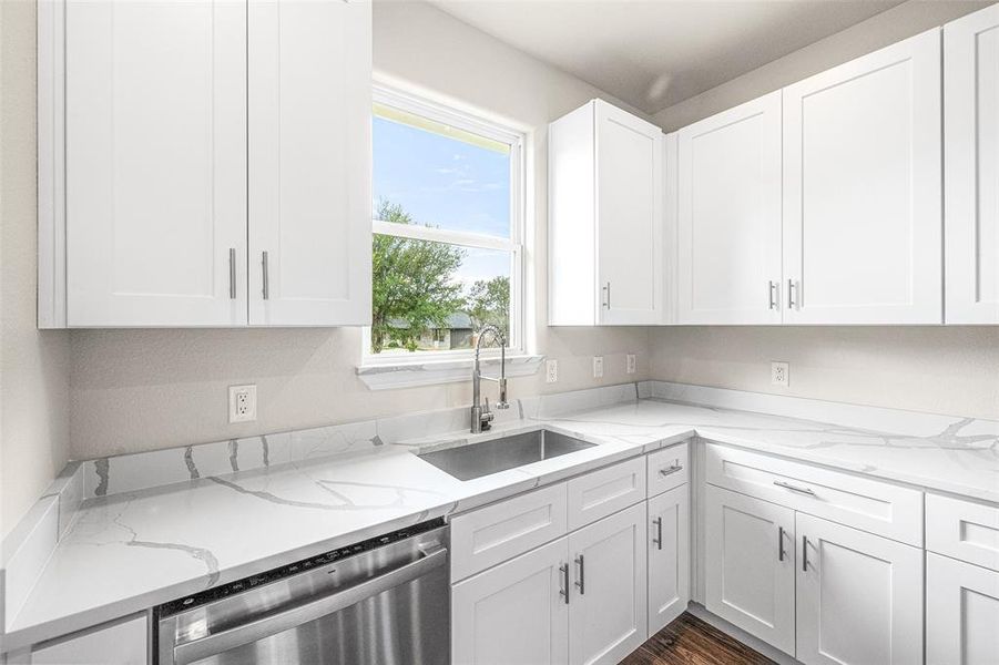 Kitchen with light stone countertops, stainless steel dishwasher, dark hardwood / wood-style flooring, sink, and white cabinets