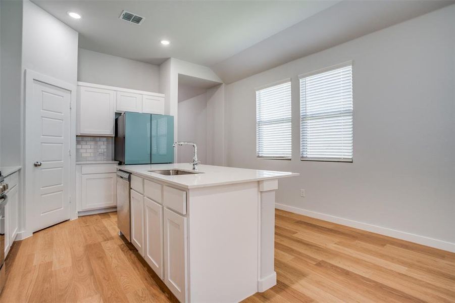 Kitchen featuring white cabinets, a center island with sink, light wood-style floors, freestanding refrigerator, and recessed lighting