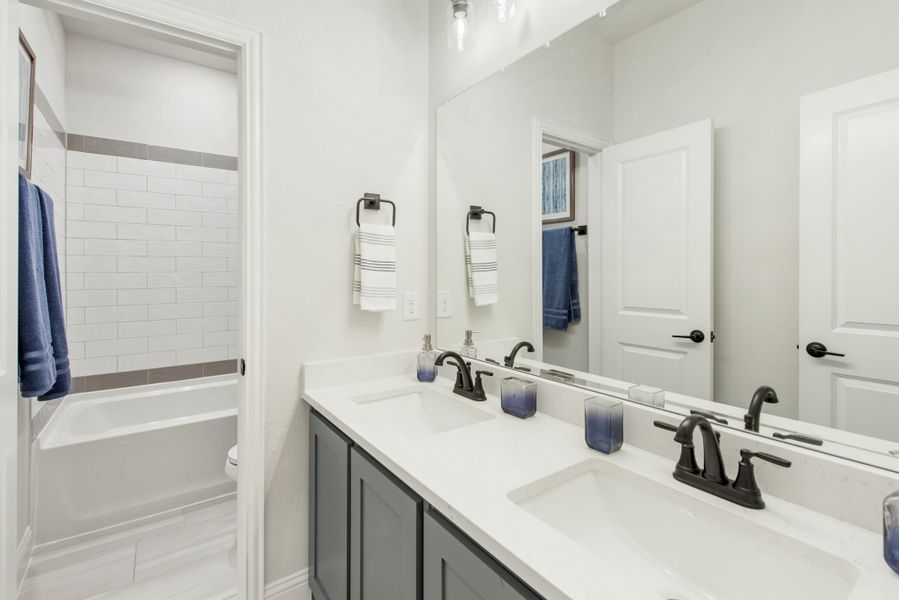Bathroom with double sink vanity, gray cabinets, large mirror, and tiled bathtub-shower combo