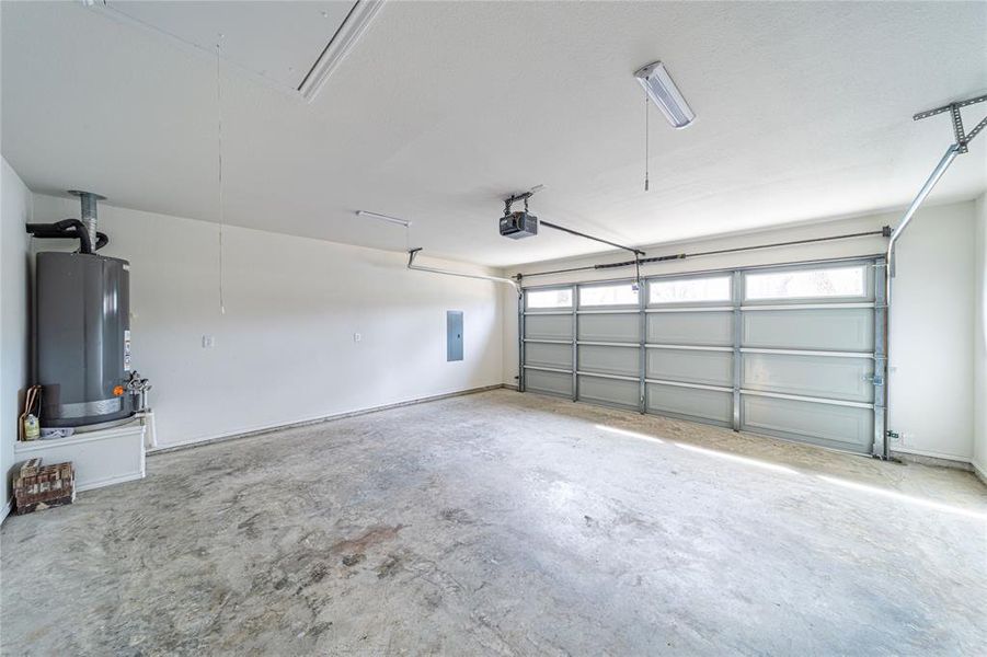 Garage with gas water heater, electric panel, and a garage door opener