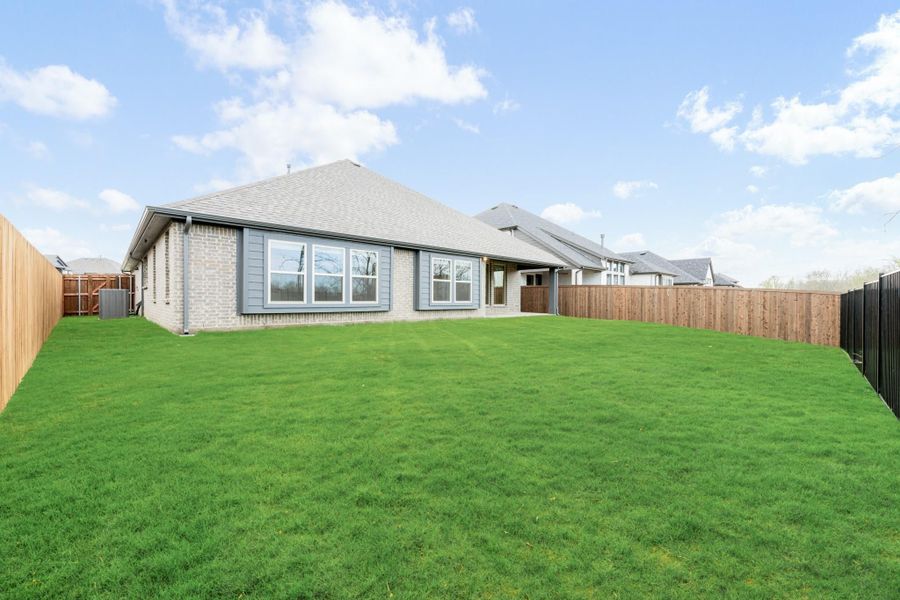 Backyard of single-story brick home with large green lawn and wood privacy fence on both sides.
