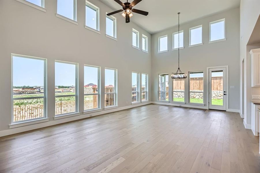 Unfurnished living room featuring ceiling fan, a towering ceiling, light wood-style floors, a chandelier, and baseboards Unfurnished living room featuring ceiling fan, a towering ceiling, light wood-style floors, a chandelier, and baseboards
