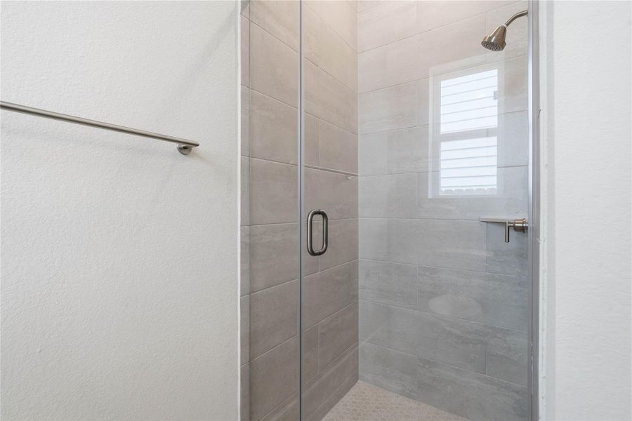 This bright secondary bathroom features a sizable walk-in shower with tile surround, vanity, mirror, and sleek modern finishes.