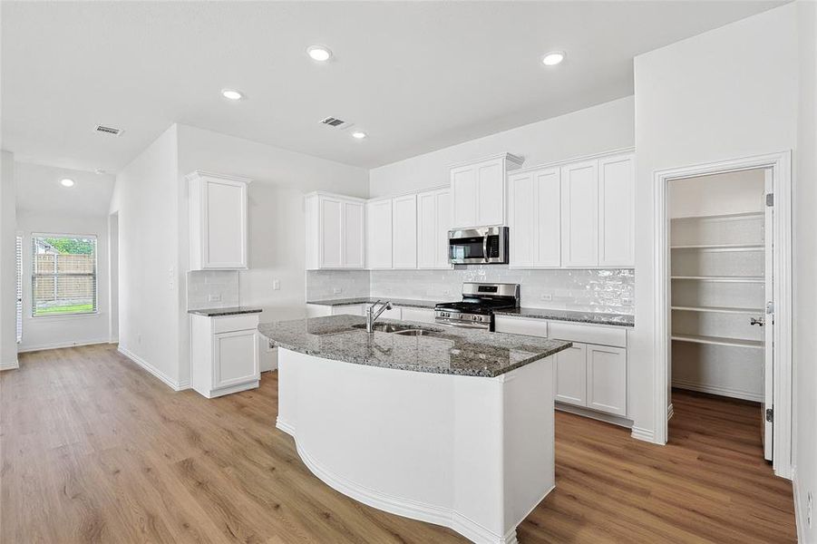 Kitchen with dark stone counters, light hardwood / wood-style flooring, stainless steel appliances, a kitchen island with sink, and white cabinetry