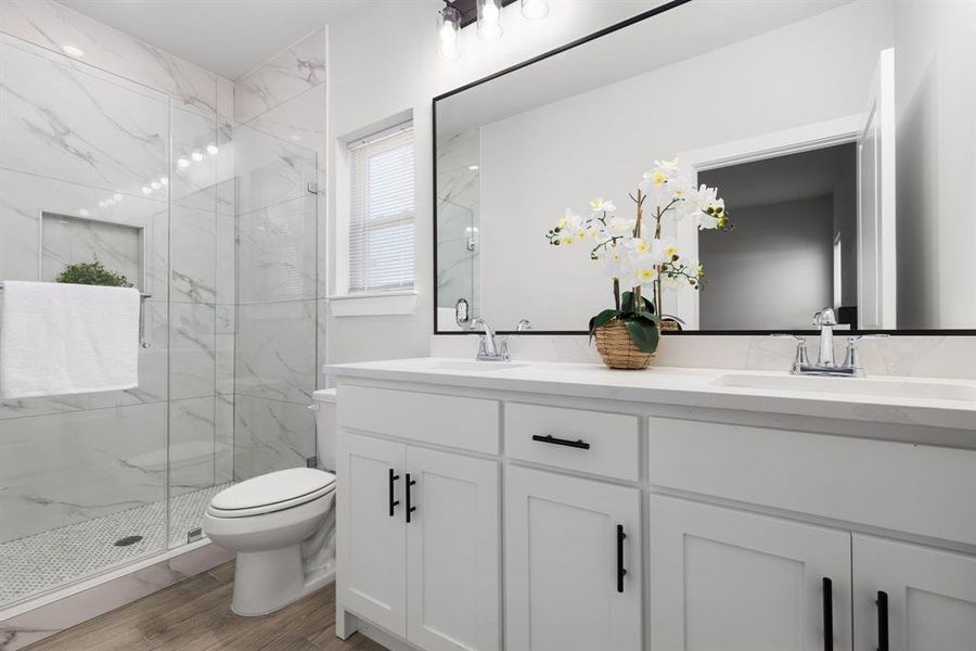 Full bathroom with toilet, wood finished floors, a sink, a marble finish shower, and double vanity