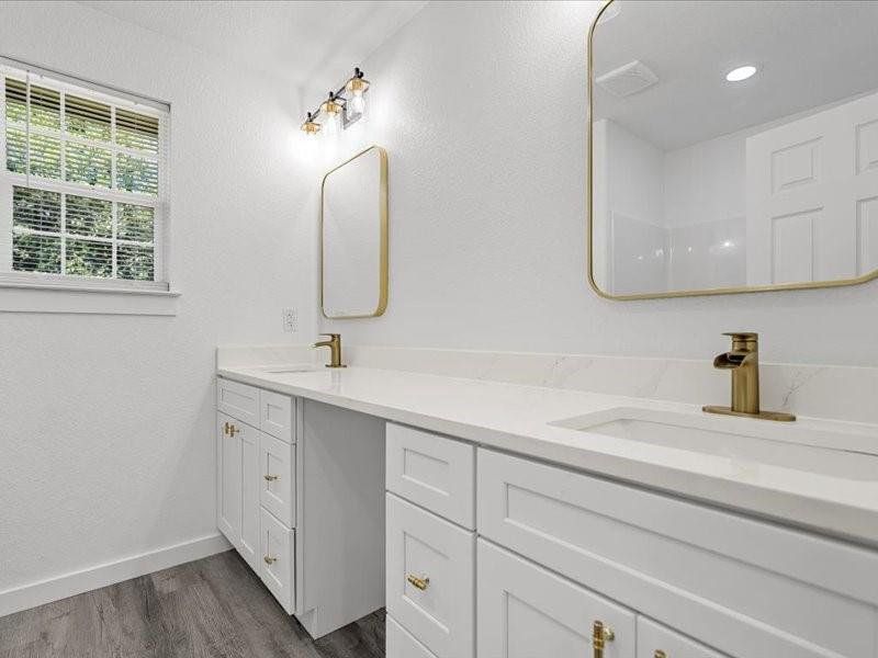 Bathroom with dark wood-style floors, double vanity, and a textured wall