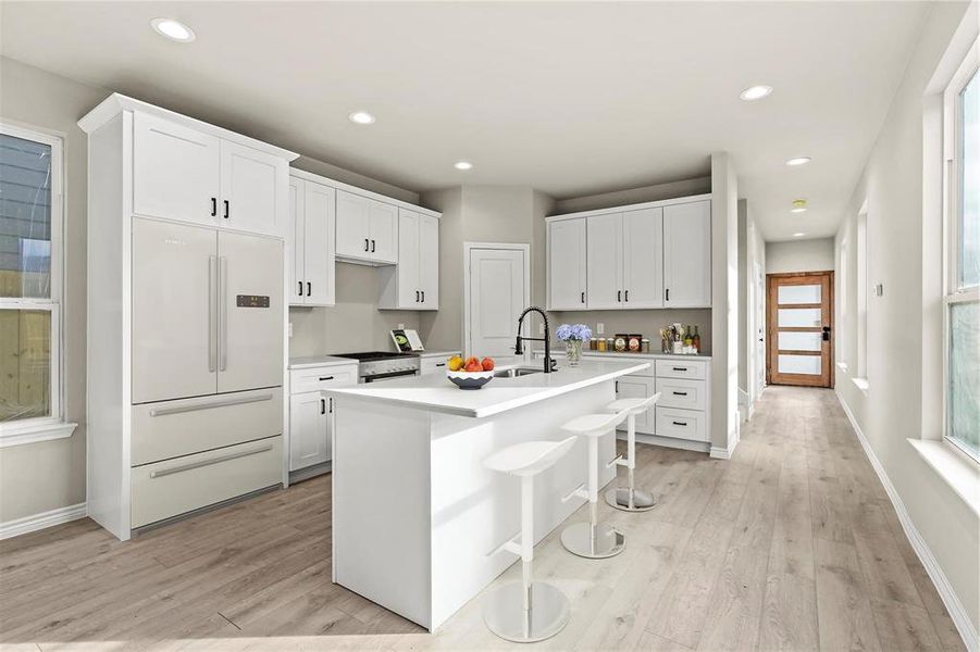 Kitchen featuring light hardwood / wood-style floors, a breakfast bar, built in refrigerator, white cabinetry, and an island with sink