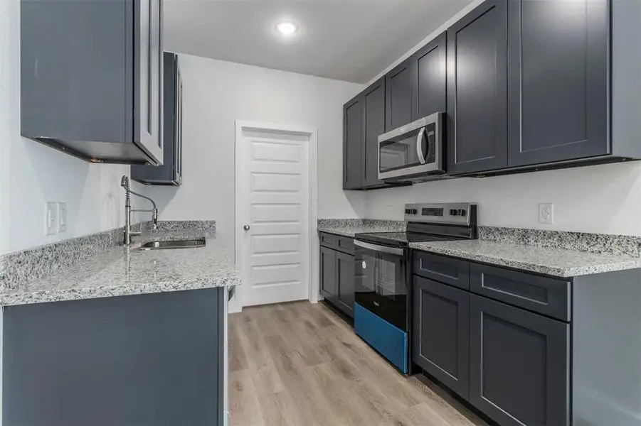 Kitchen featuring light stone countertops, appliances with stainless steel finishes, light hardwood / wood-style flooring, and sink