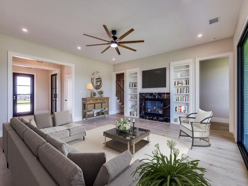 Virtual Staged Living room featuring light wood flooring, a marble surround fireplace, ceiling fan, baseboards, and recessed lighting, built in bookcases with hidden storage, triple pane sliding glass doors for access to covered patio