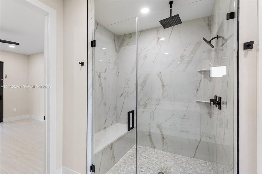 LUXURIOUS PRIMARY BATHROOM w/ spacious WALK-IN GLASS SHOWER w/ floor-to-ceiling designer tile, rainfall showerhead, built-in bench & modern matte-black fixtures.