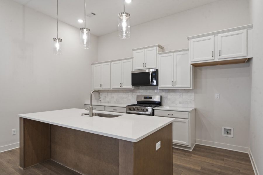 Kitchen featuring a central island with a solid surface countertop, white cabinetry with crown molding, stainless steel appliances, a tile backsplash, and wood-finish flooring Kitchen featuring a central island with a solid surface countertop, white cabinetry with crown molding, stainless steel appliances, a tile backsplash, and wood-finish flooring