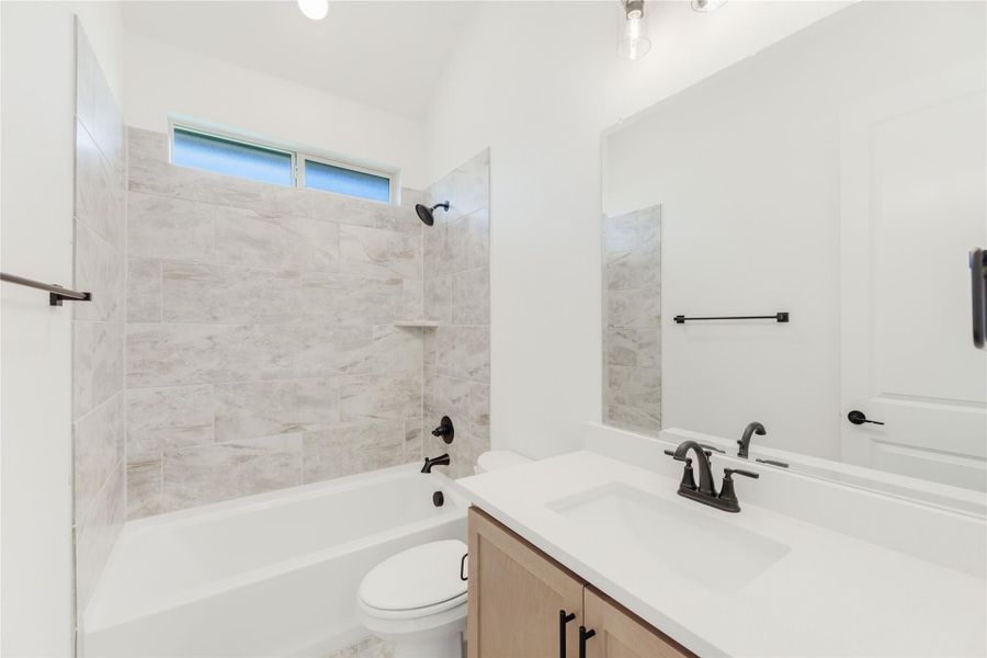 Bathroom with tiled tub-shower combo, white vanity, wood cabinets, and black fixtures