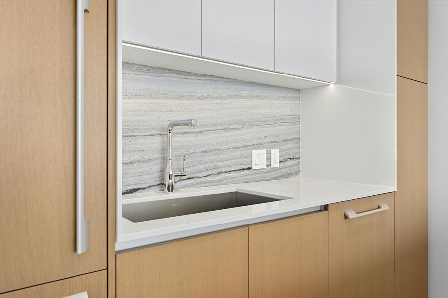 The kitchen features a sleek, minimalist design with clean-lines cabinetry that combines light wood finishes and white fronts. The backsplash matches the island countertop, creating a cohesive and sophisticated look.