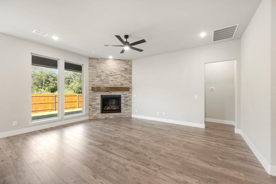 Open living room with stone fireplace, wood mantel, hardwood floors, and ceiling fan