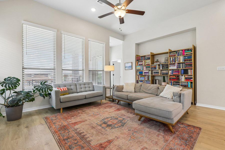 A naturally illuminated living room features built-in shelving, high ceilings, and light wood flooring.