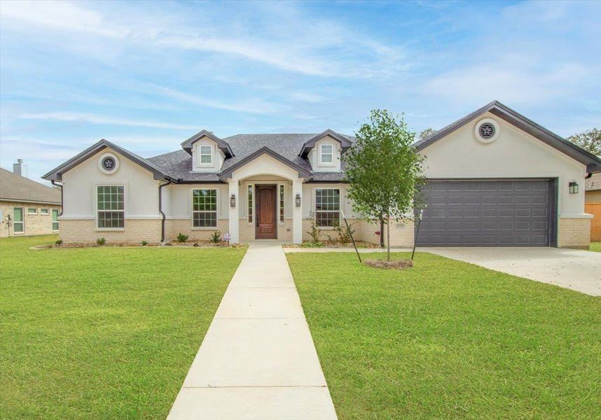 View of front facade with a garage, driveway, a front yard, brick siding, and stucco siding View of front facade with a garage, driveway, a front yard, brick siding, and stucco siding