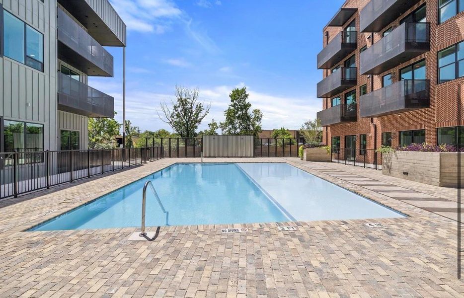 An inviting swimming pool is situated in a paved courtyard between modern multi-family buildings. An inviting swimming pool is situated in a paved courtyard between modern multi-family buildings.