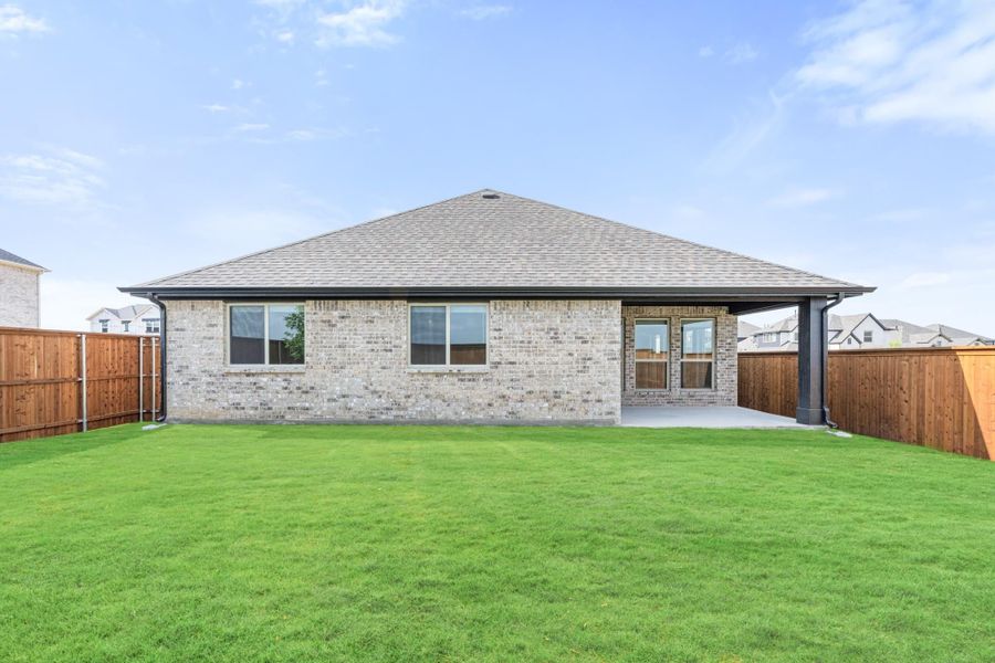 Rear view of single-story brick home with covered patio, green lawn, and wood privacy fence Rear view of single-story brick home with covered patio, green lawn, and wood privacy fence