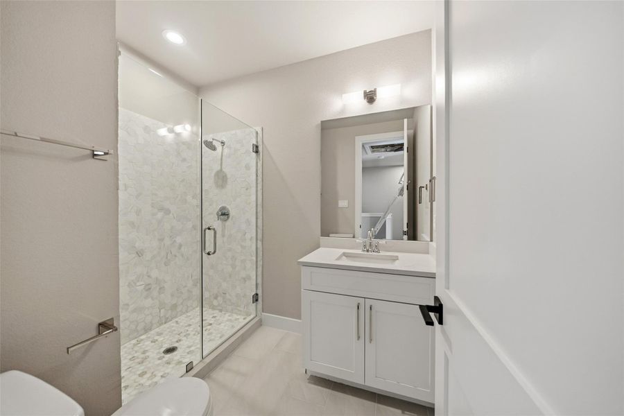 This bathroom features a modern design with a glass-enclosed shower, elegant white vanity, and contemporary fixtures. The neutral color palette and recessed lighting create a bright and inviting space.