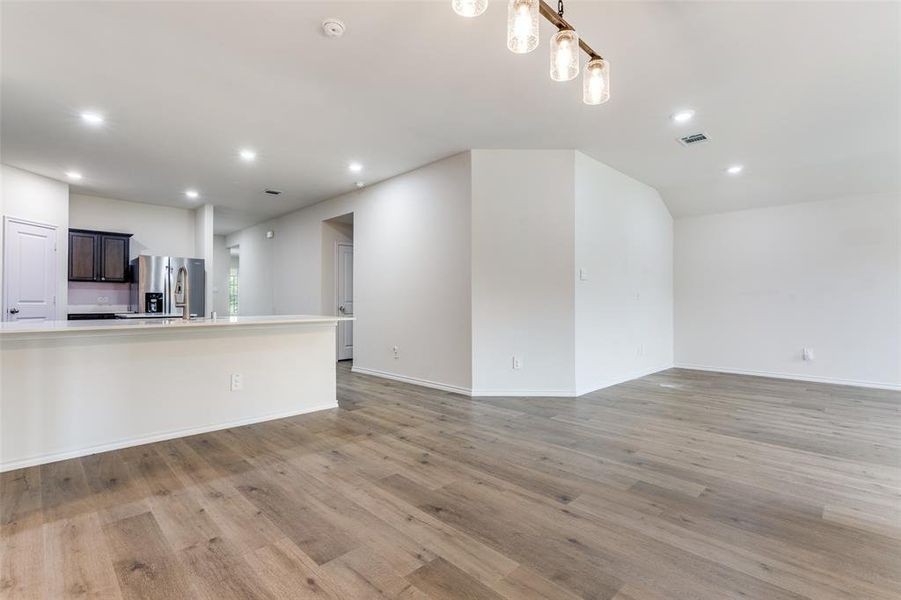 Open-concept living area with wood-finish flooring, recessed lighting, and a modern chandelier Open-concept living area with wood-finish flooring, recessed lighting, and a modern chandelier