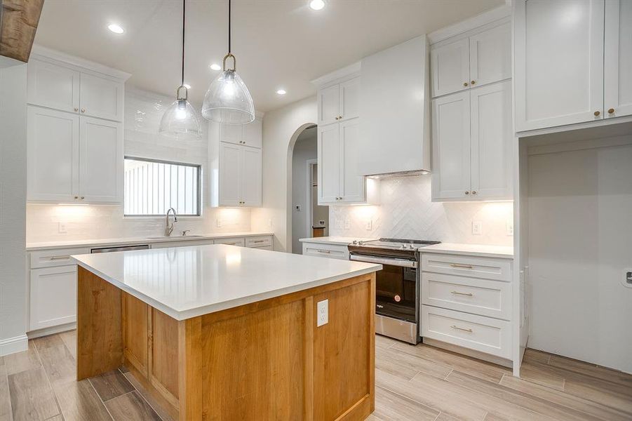 Kitchen featuring white cabinets, stainless steel electric range oven, hanging light fixtures, brown cabinets, and a kitchen island Kitchen featuring white cabinets, stainless steel electric range oven, hanging light fixtures, brown cabinets, and a kitchen island