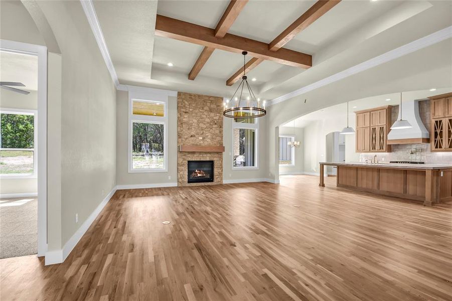Unfurnished living room featuring arched walkways, beamed ceiling, a fireplace, a chandelier, and light wood-type flooring