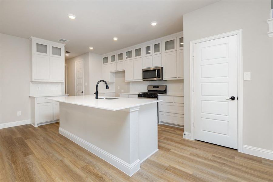 Kitchen featuring white cabinetry, recessed lighting, gas range, stainless steel microwave, and glass insert cabinets
