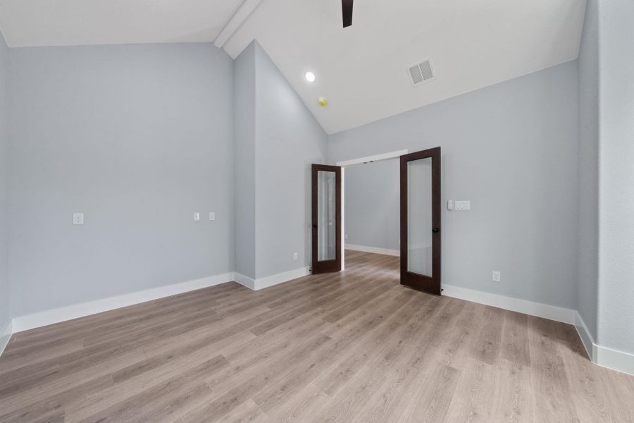 Spacious room featuring vaulted ceilings, wood-finish flooring, recessed lighting, and a pair of dark wood French doors with frosted glass panels