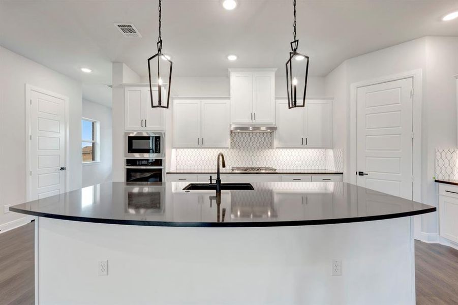 Kitchen with dark wood-style flooring, white cabinets, tasteful backsplash, stainless steel appliances, and pendant lighting