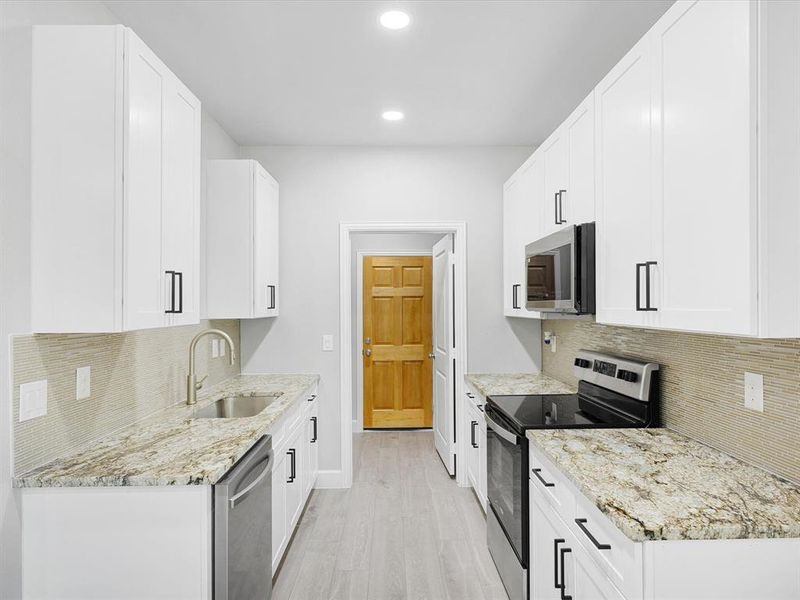 Kitchen with stainless steel appliances, light stone countertops, white cabinets, and recessed lighting