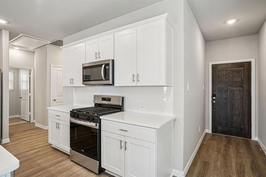 Kitchen featuring stainless steel appliances, recessed lighting, white cabinets, light wood-style floors, and tasteful backsplash