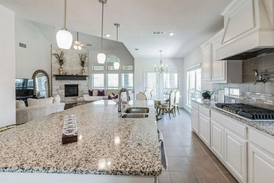 Kitchen with a stone fireplace, sink, white cabinetry, a large island with sink, and custom exhaust hood