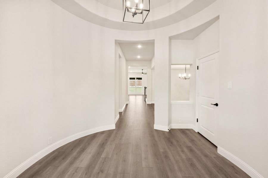 Curved entryway with round tray ceiling, pendant light fixture, and dark hardwood floors leading to hallway