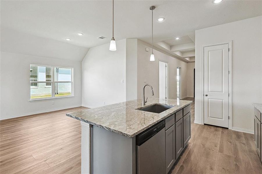 Kitchen with sink, light hardwood / wood-style floors, decorative light fixtures, stainless steel dishwasher, and light stone counters