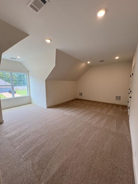 Spacious room featuring vaulted ceilings, recessed lighting, neutral-toned carpet, and a large window providing ample natural light